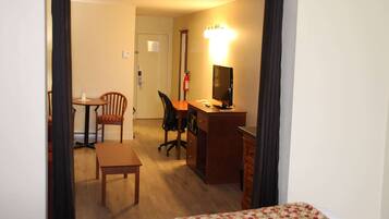 A hotel room with a bed, a desk with a computer, a chair, a small table, and a fire extinguisher.