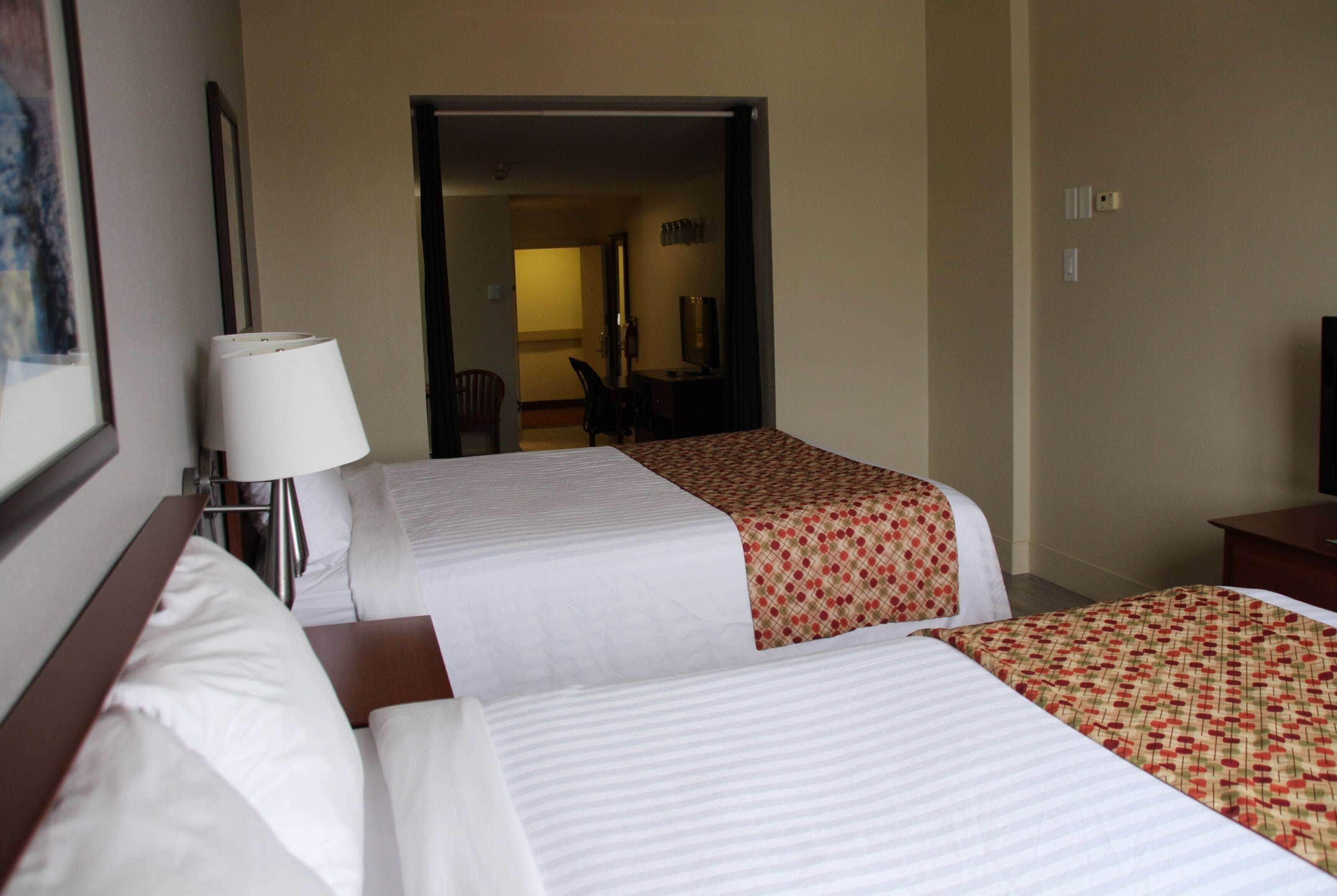 Quarto de hotel com duas camas, uma escrivaninha, uma cadeira e uma televisão.