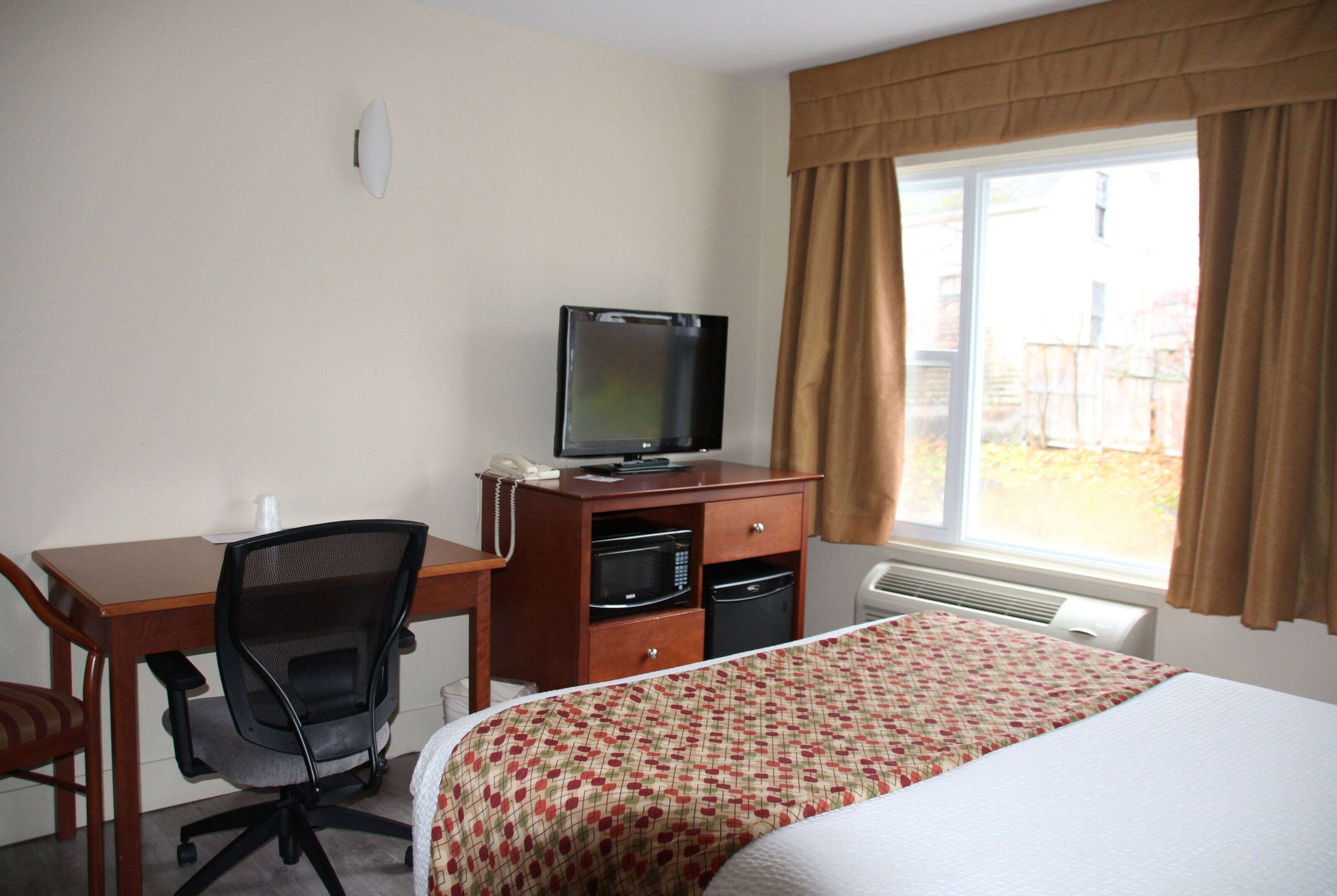 A hotel room with a bed, a desk with a computer, a chair, a television, and a window with curtains.
