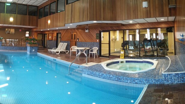 Una piscina interior con sillas de descanso, un jacuzzi y equipo de ejercicio.