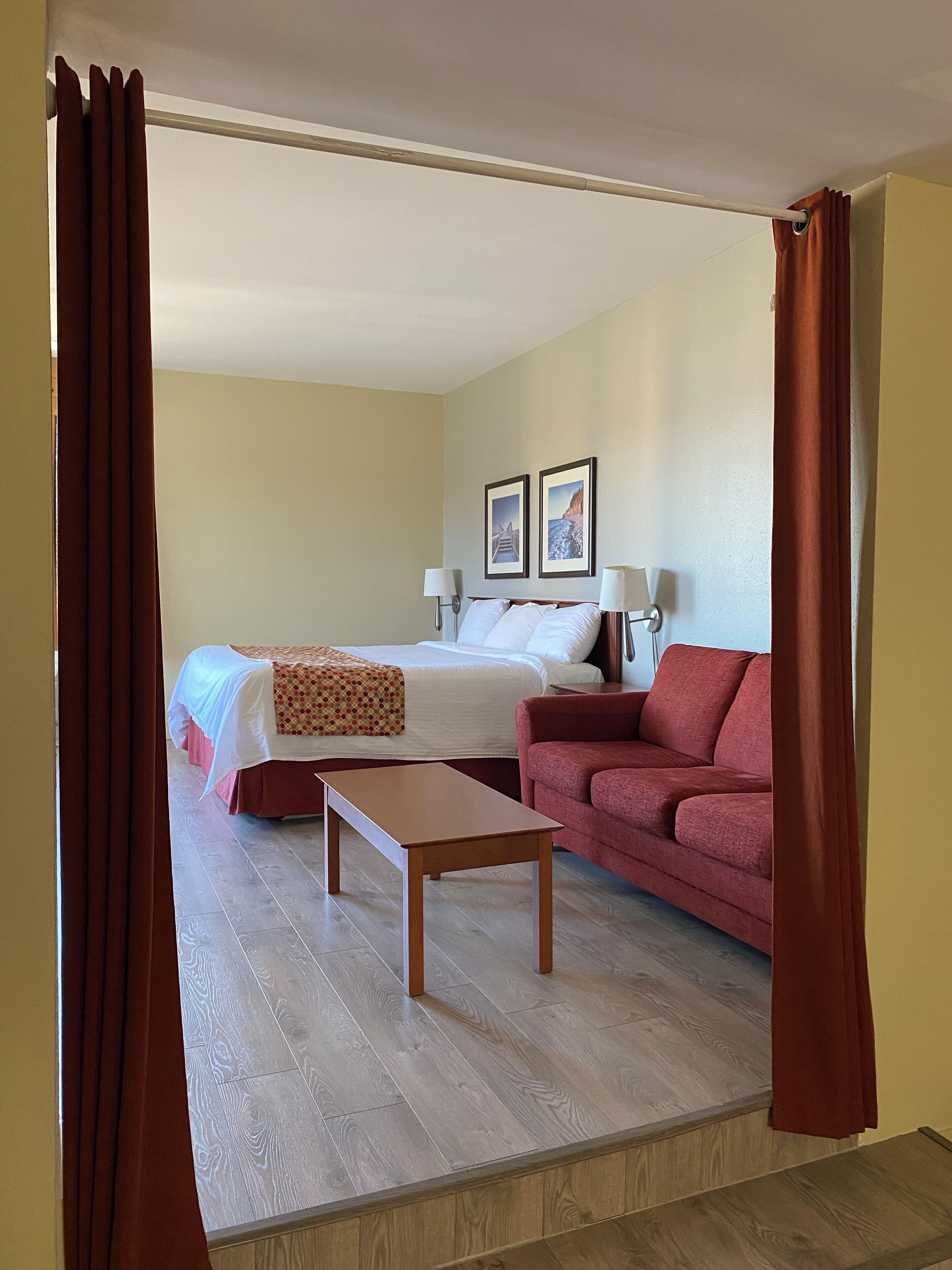 A hotel room with a bed, a red sofa, a wooden table, and two wall-mounted lamps.