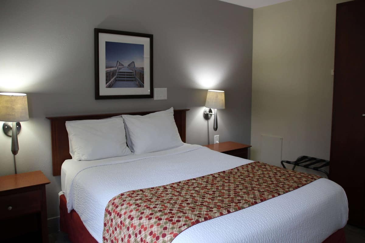 A hotel room with a large bed, two bedside lamps, a framed picture on the wall, and a door to the right.