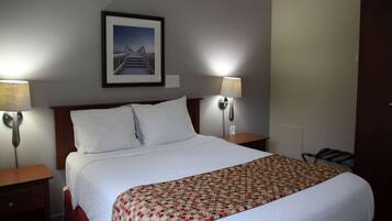 A hotel room with a large bed, two bedside lamps, a framed picture on the wall, and a door to the right.