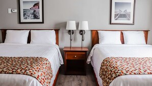 Habitación de hotel con dos camas, una mesita de noche con dos lámparas y cuadros enmarcados en la pared.