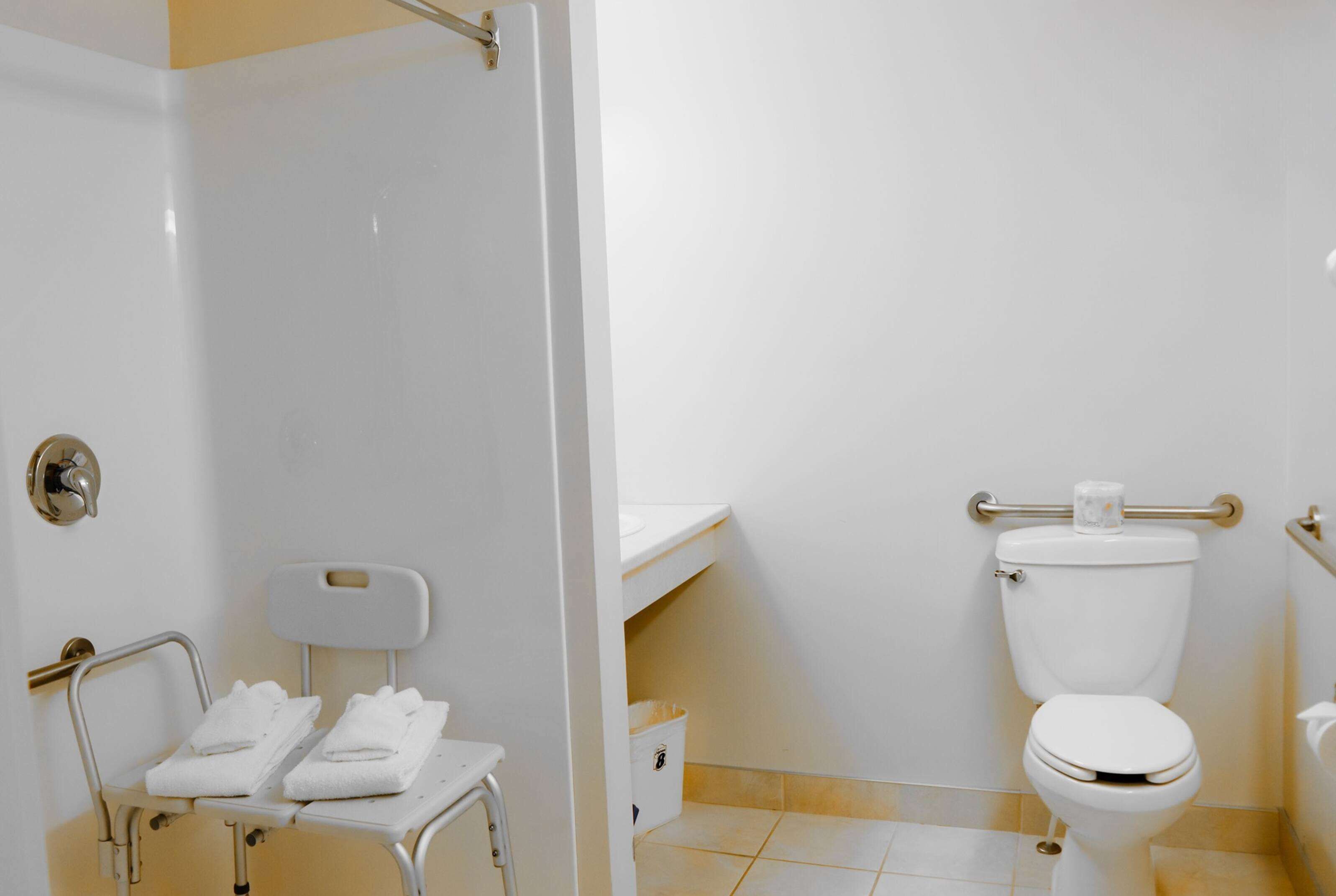 Un bagno con un water bianco, zona doccia e una panca accessibile in sedia a rotelle con asciugamani.