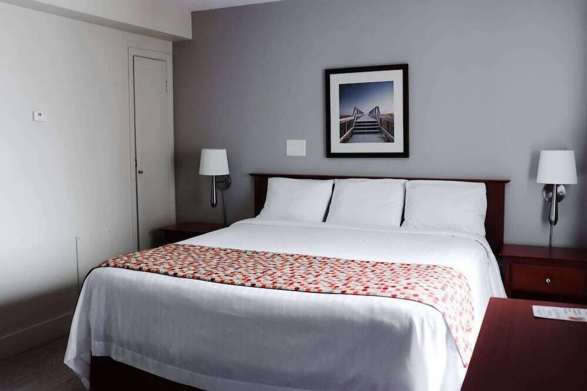 Habitación de hotel con cama, dos lámparas de noche, un cuadro en la pared y una puerta.