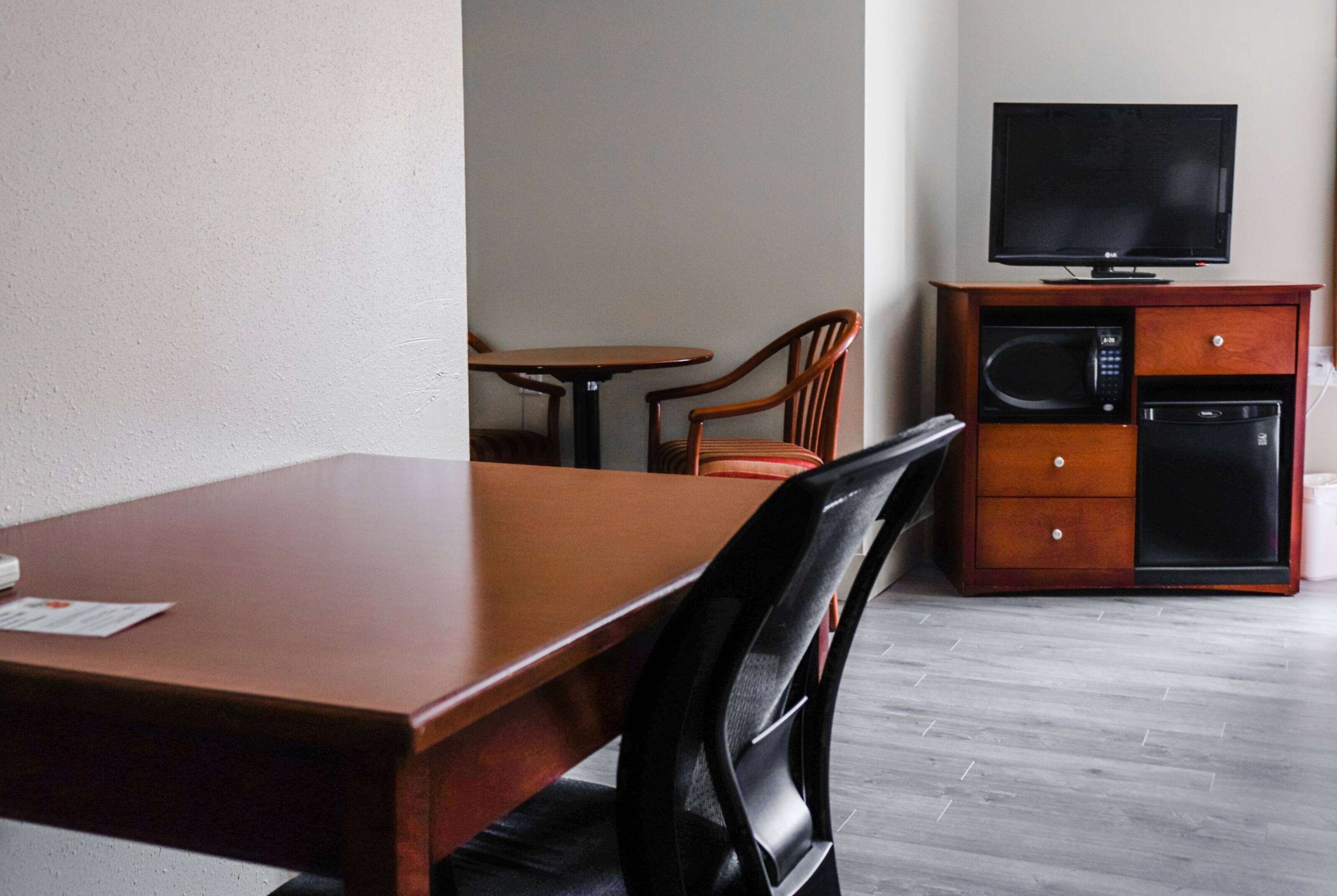 A hotel room with a wooden dining table, two chairs, a television on a wooden cabinet, and a microwave.