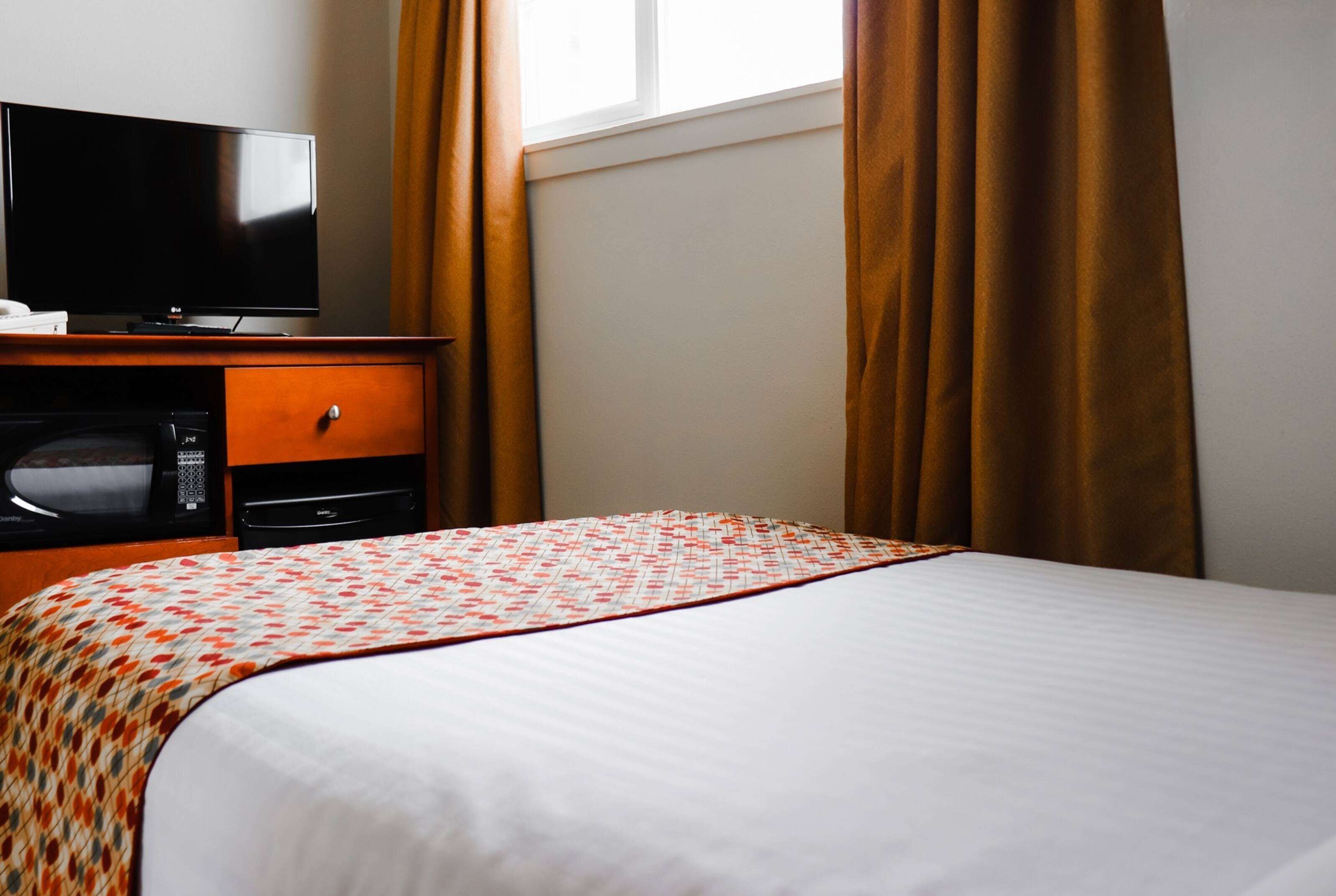 A hotel room with a bed, a television, a microwave, and a dresser.