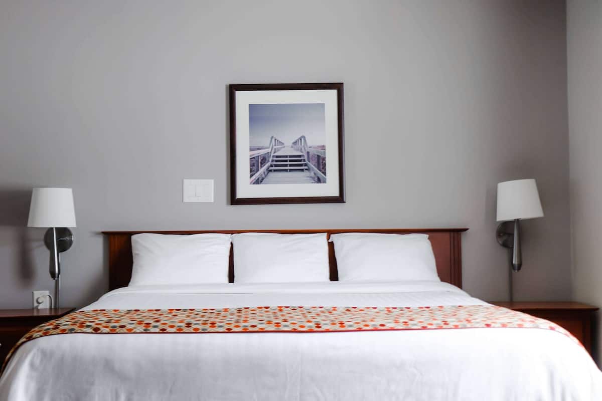 A hotel room with a bed, two bedside lamps, a framed picture on the wall, and a patterned bedspread.