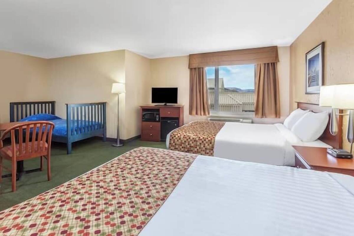 A hotel room with two beds, a desk, a TV, and a window with a view of a building.