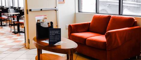 A modern interior with a red sofa, a wooden table with a menu, and a checkered floor.