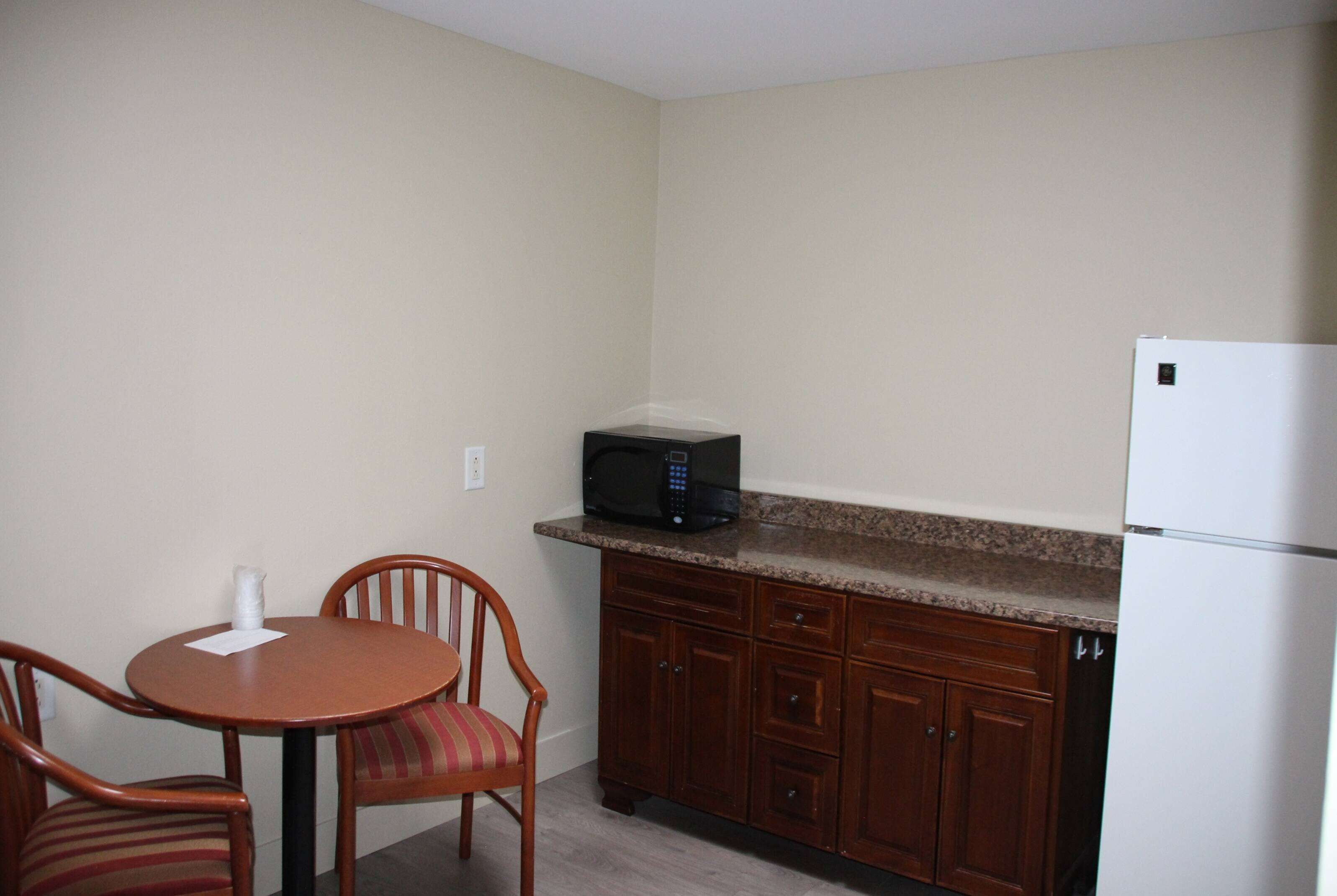 A small kitchen with a microwave, a refrigerator, wooden cabinets, and a dining table with chairs.