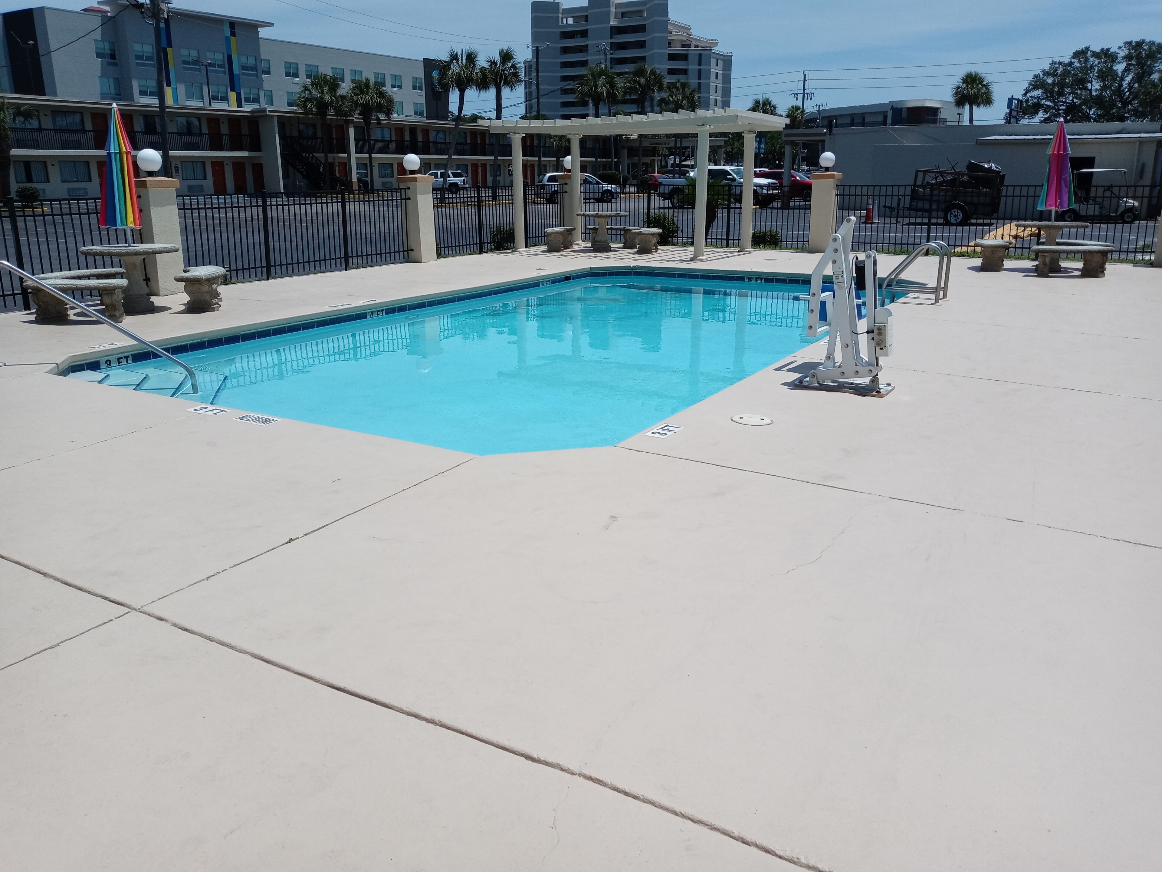 Une piscine à l’eau d’un bleu limpide, entourée d’une terrasse en béton et d’une clôture en métal.