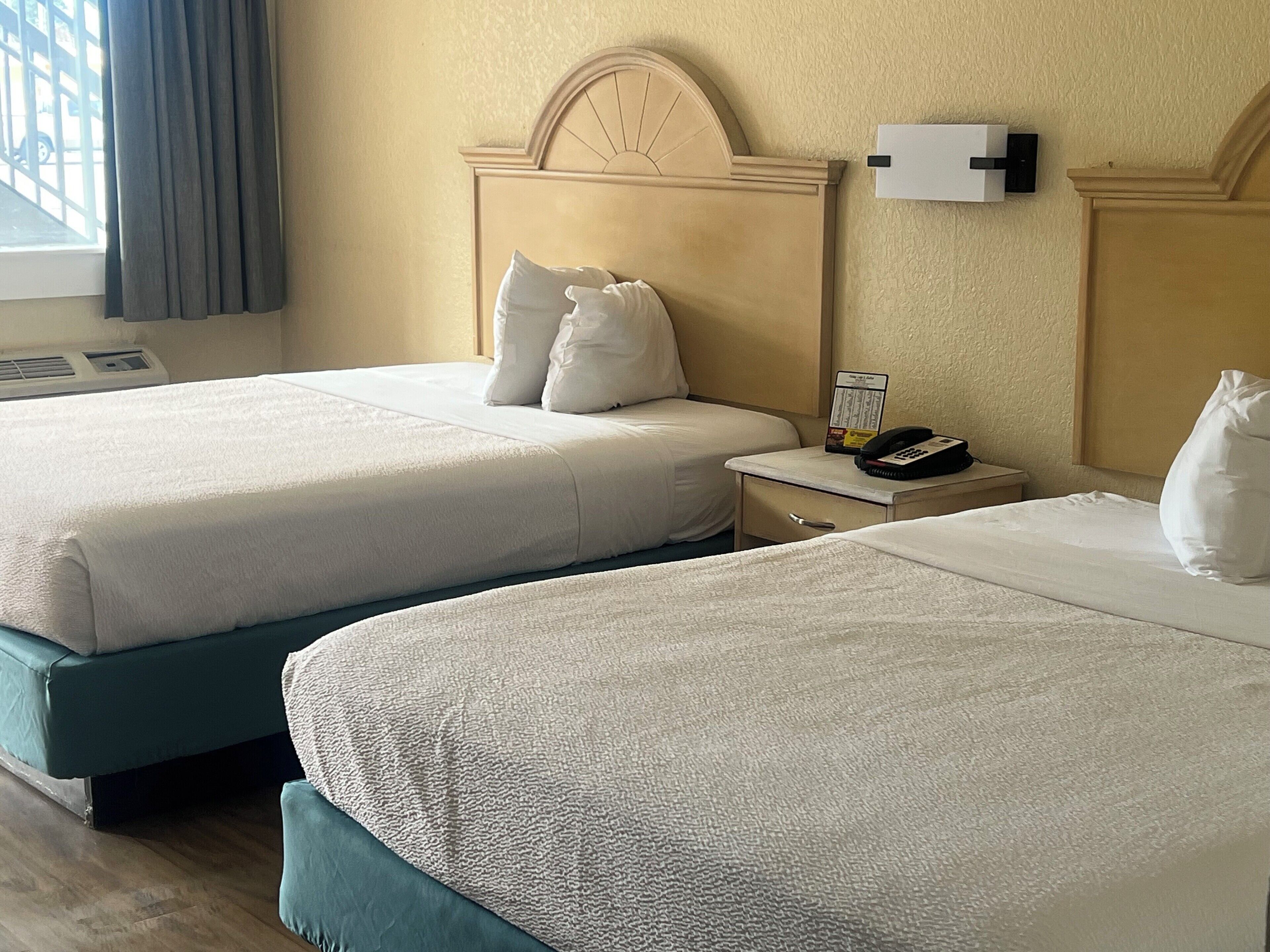Een hotelkamer met twee bedden, een nachtkastje met een telefoon en een kaart, en een raam met gordijnen.