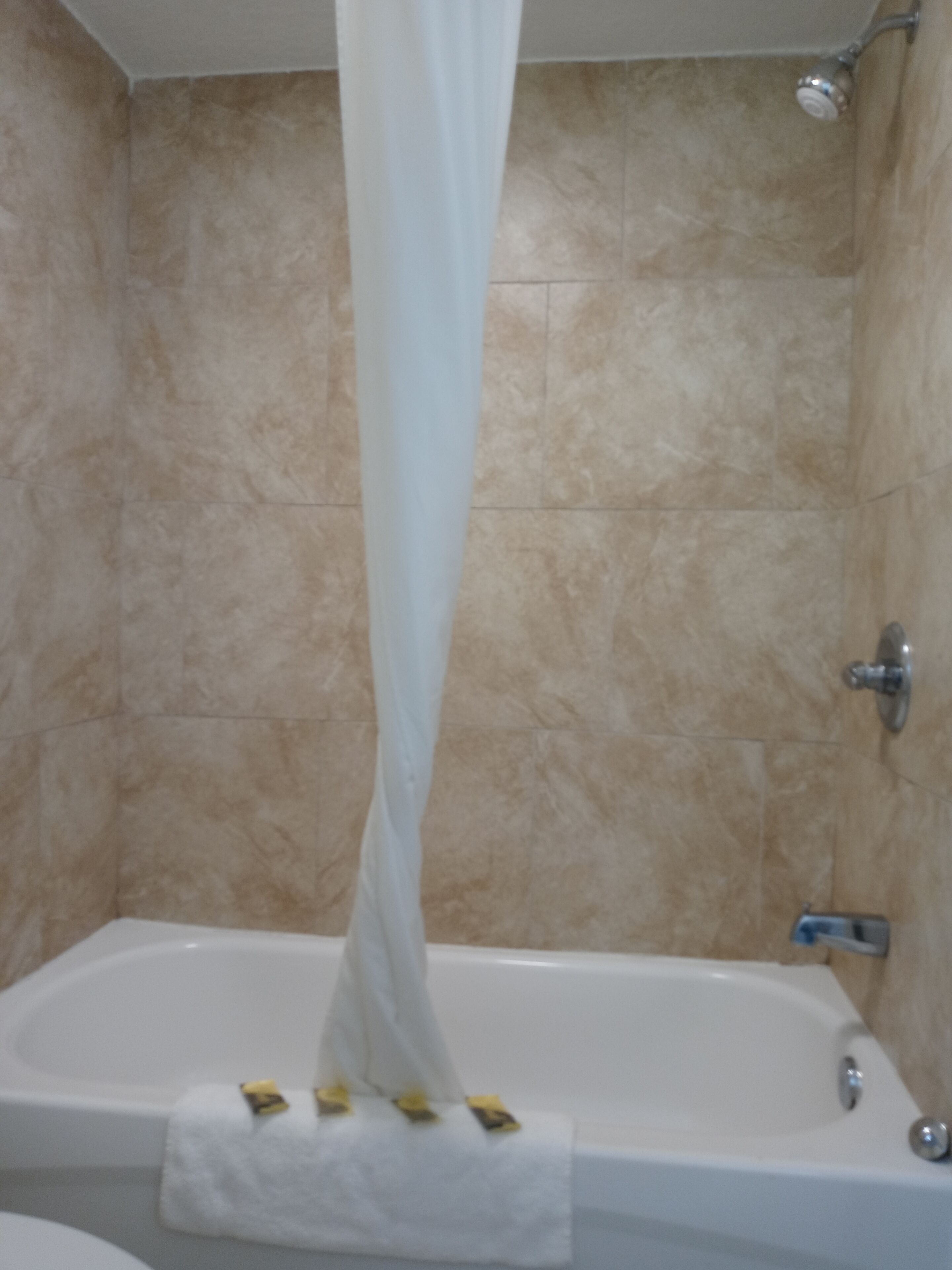 Un baño con bañera, ducha y paredes con azulejos color beige.