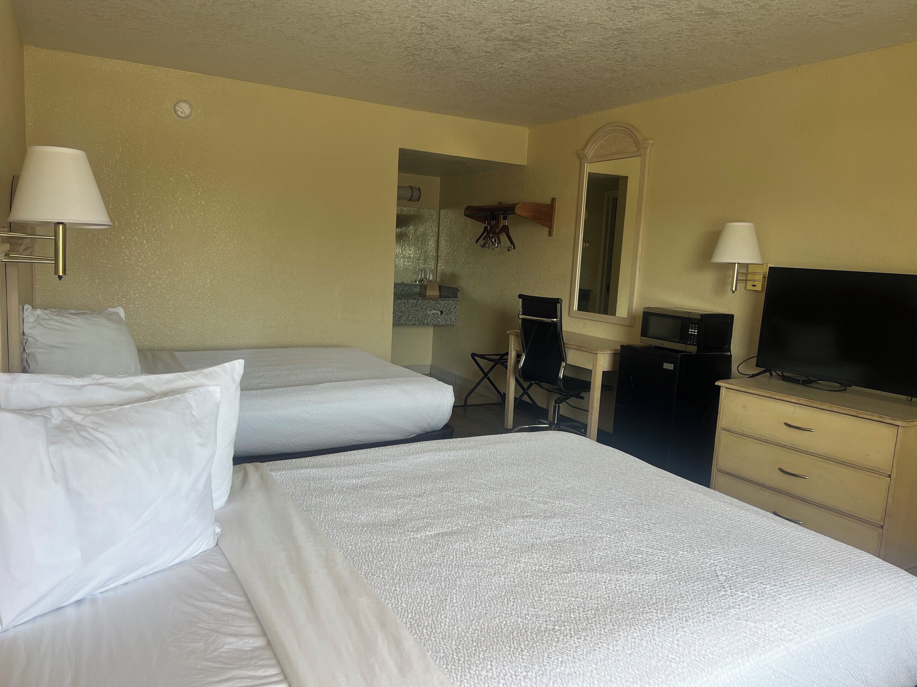 A hotel room with two beds, a desk with a chair, a television, and a mirror.