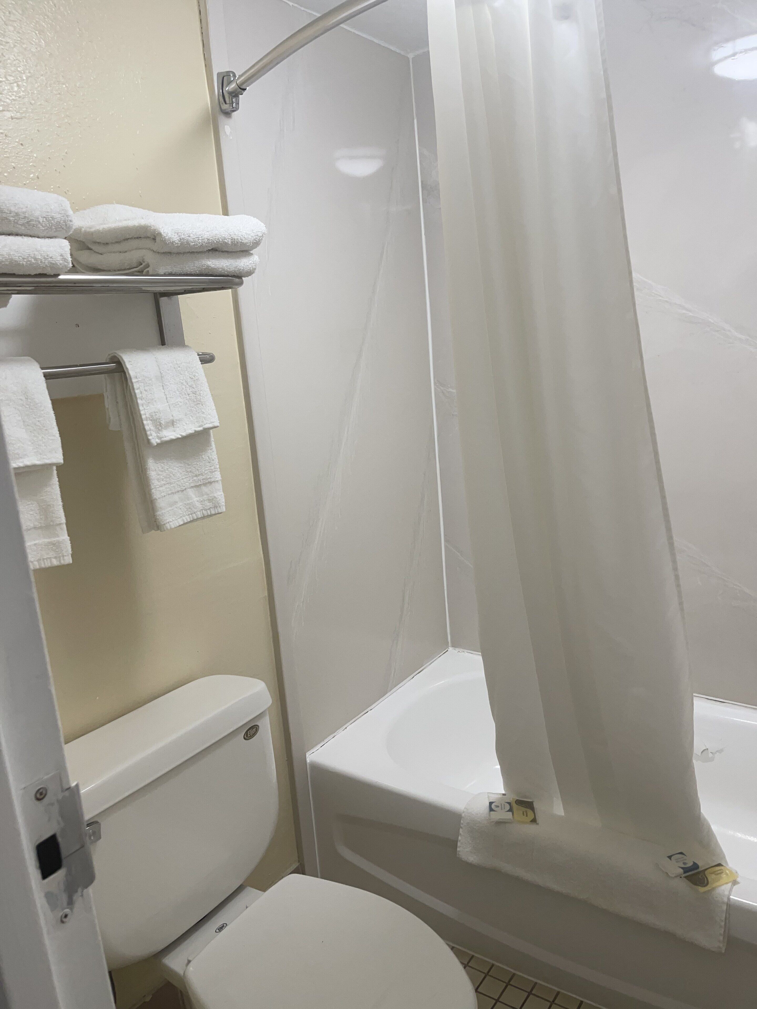 A bathroom with a toilet, a shower with a curtain, and a towel rack with folded towels.