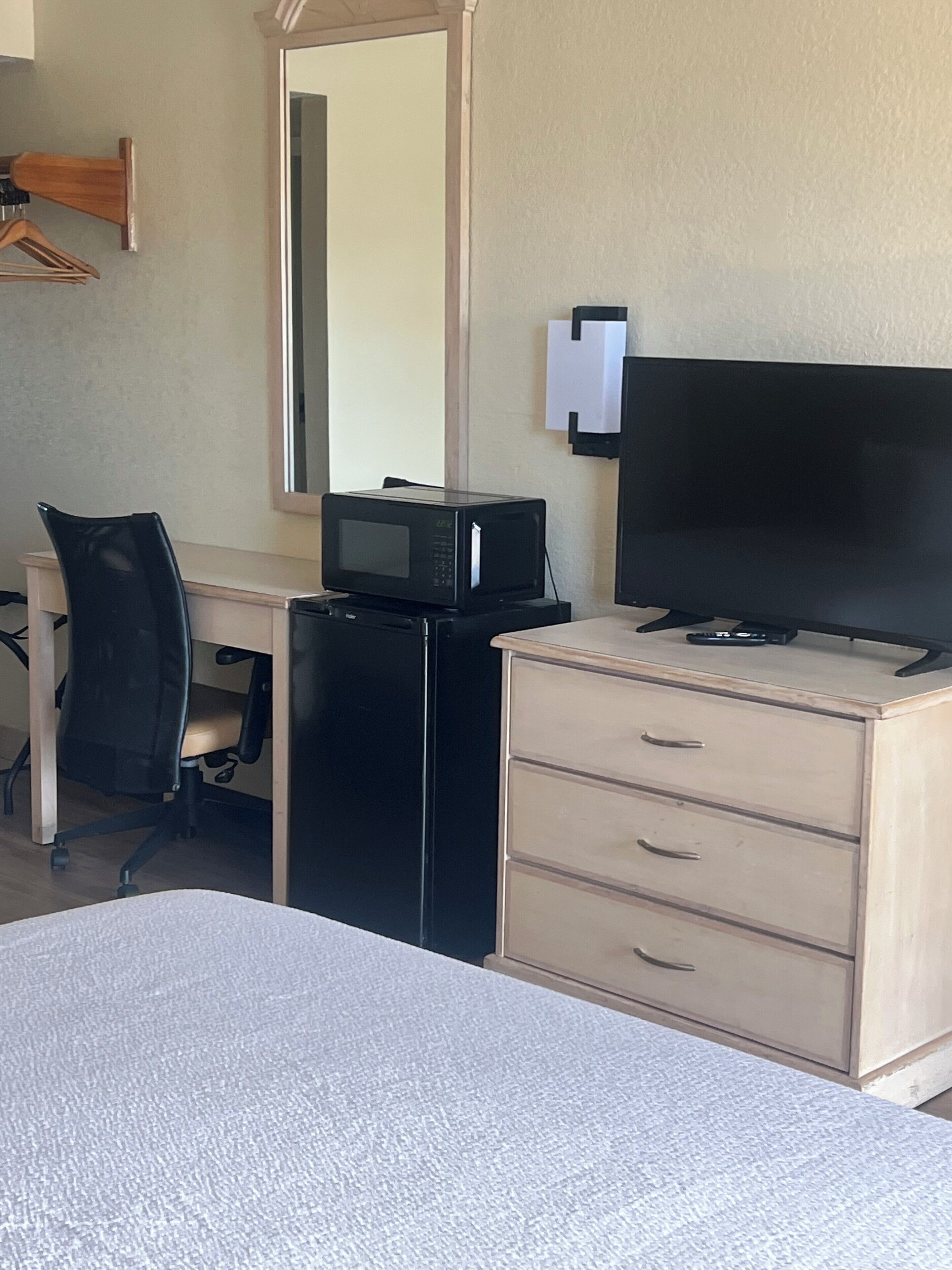A hotel room with a bed, a desk with a computer, a microwave, a television, and a dresser.