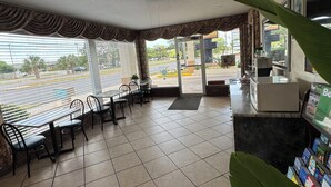 Un restaurante con vista a una calle y palmeras. Hay mesas y sillas en su interior.