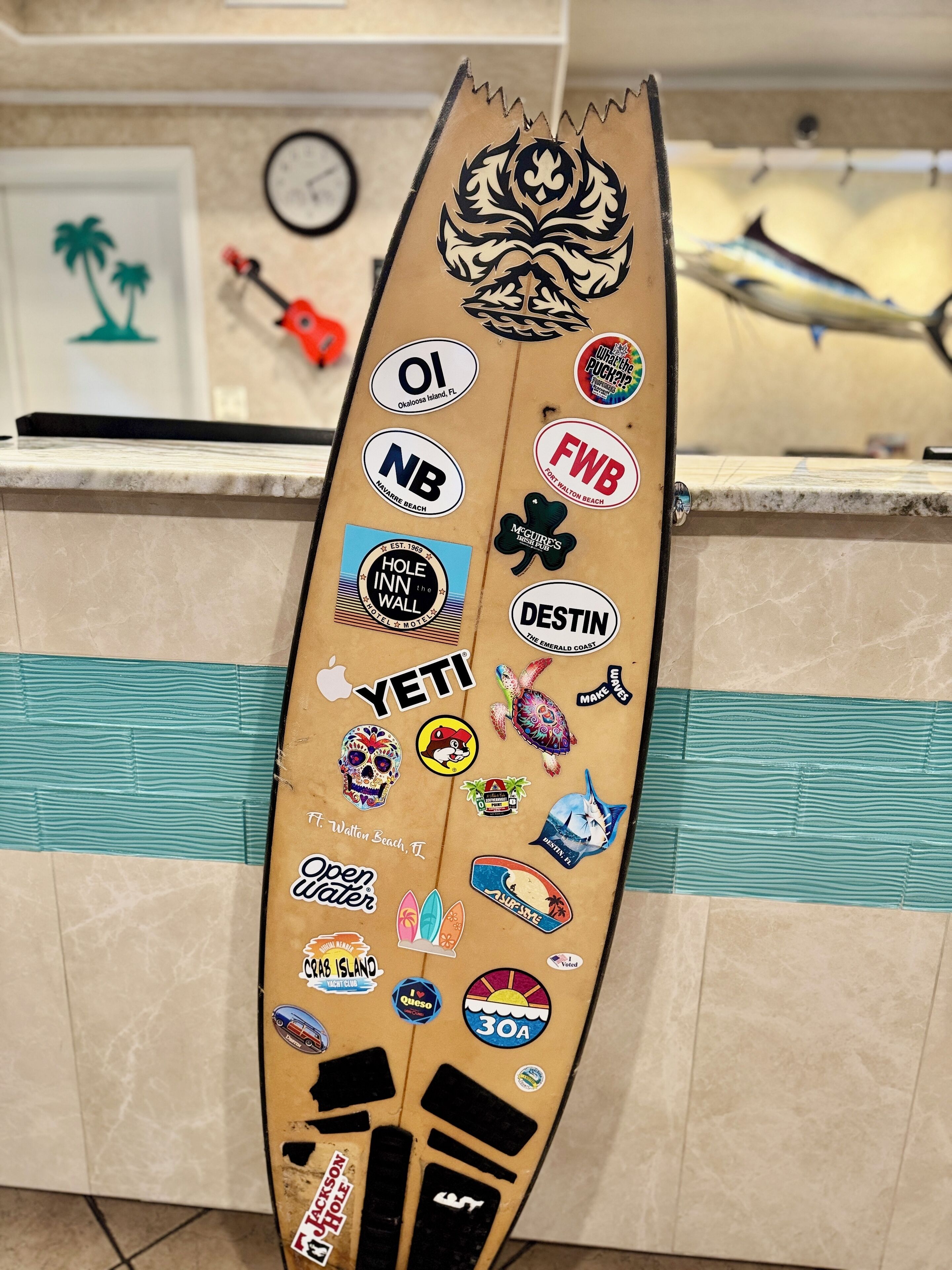 A surfboard with various stickers and logos, including "YETI," "Destin," and "Open Water."