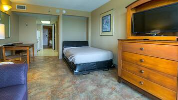 A hotel room with a bed, a wooden dresser, a television, a desk, and a chair.