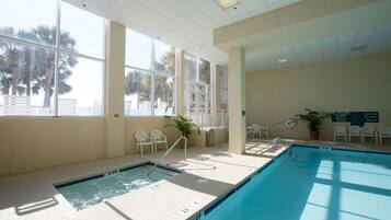 An indoor swimming pool with clear water, surrounded by white chairs and a potted plant.