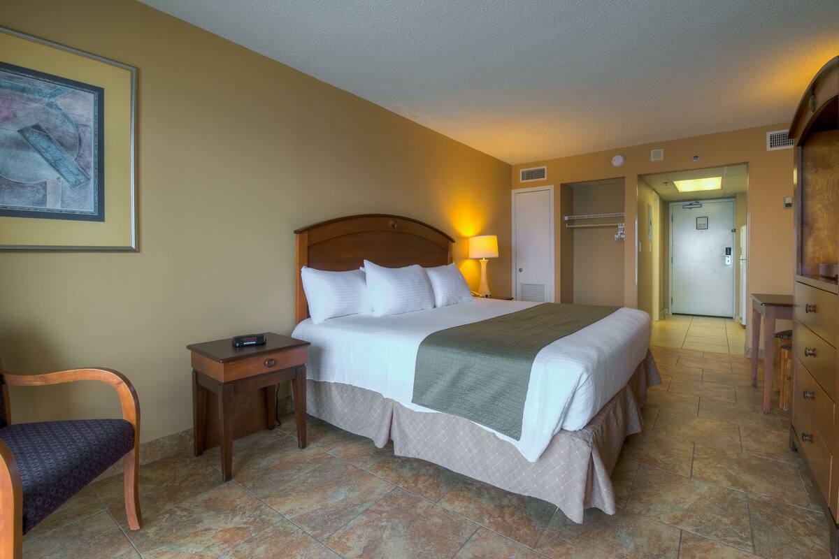 A hotel room with a bed, a chair, a nightstand, a lamp, and a door leading to a bathroom.