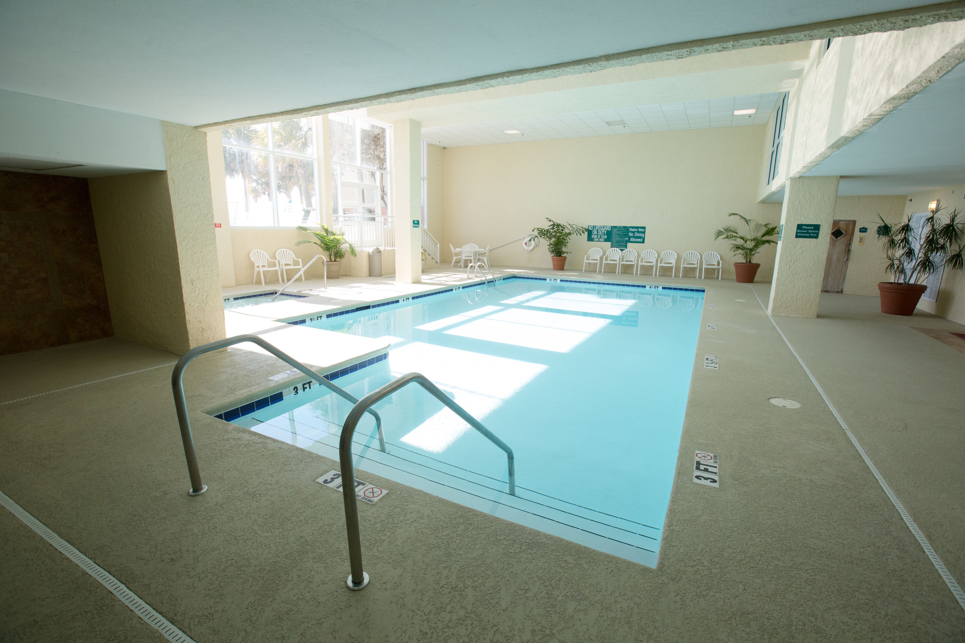 An indoor swimming pool with clear water, a lifeguard chair, and potted plants.