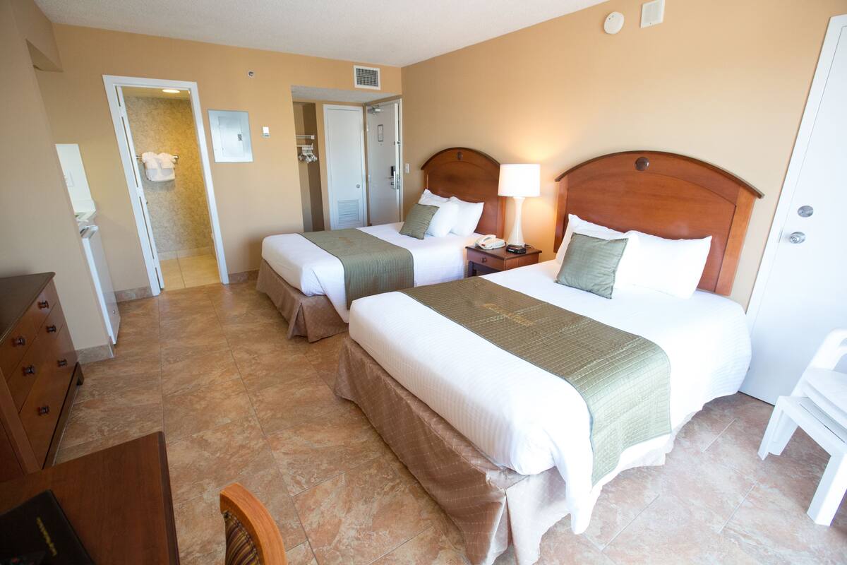 A hotel room with two beds, a desk, and a chair.