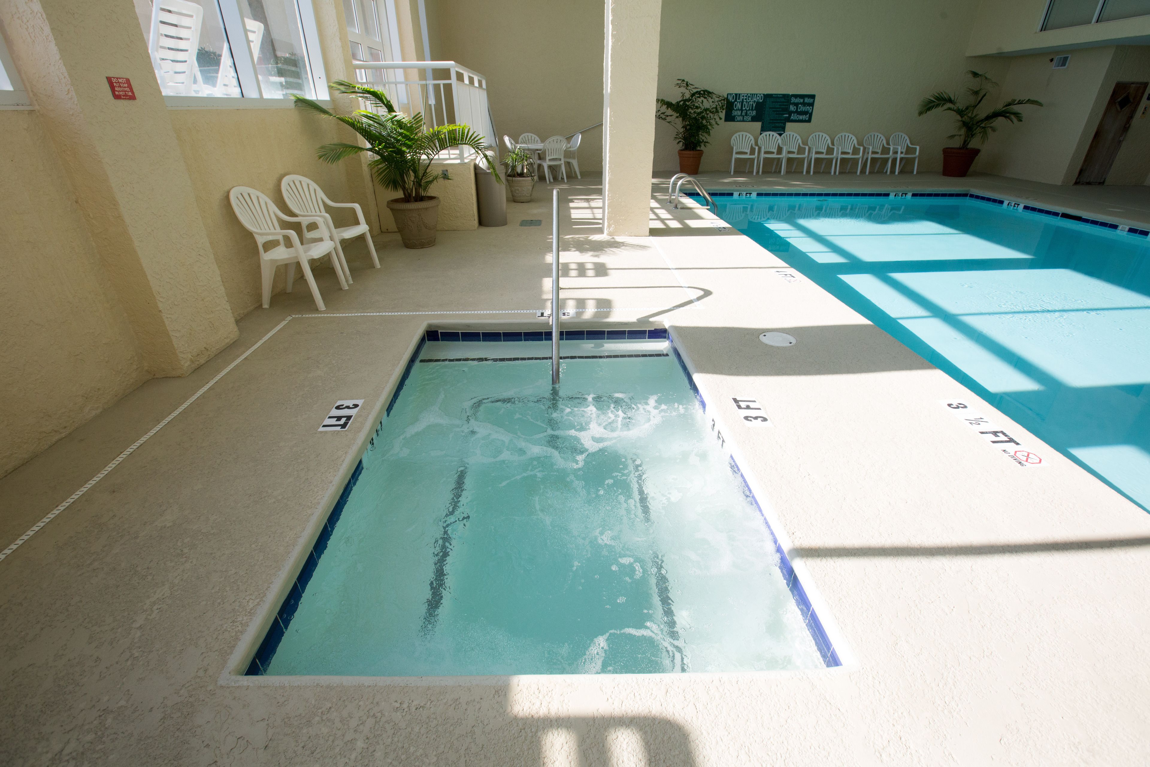 An indoor swimming pool with clear water, surrounded by white chairs and potted plants.