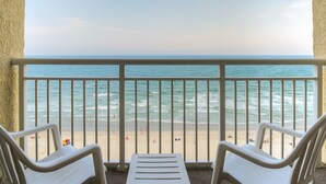 A balcony with two white chairs facing a beach with people and a lifeguard tower. - Ocean Drive Beach & Golf Resort (North Myrtle Beach)