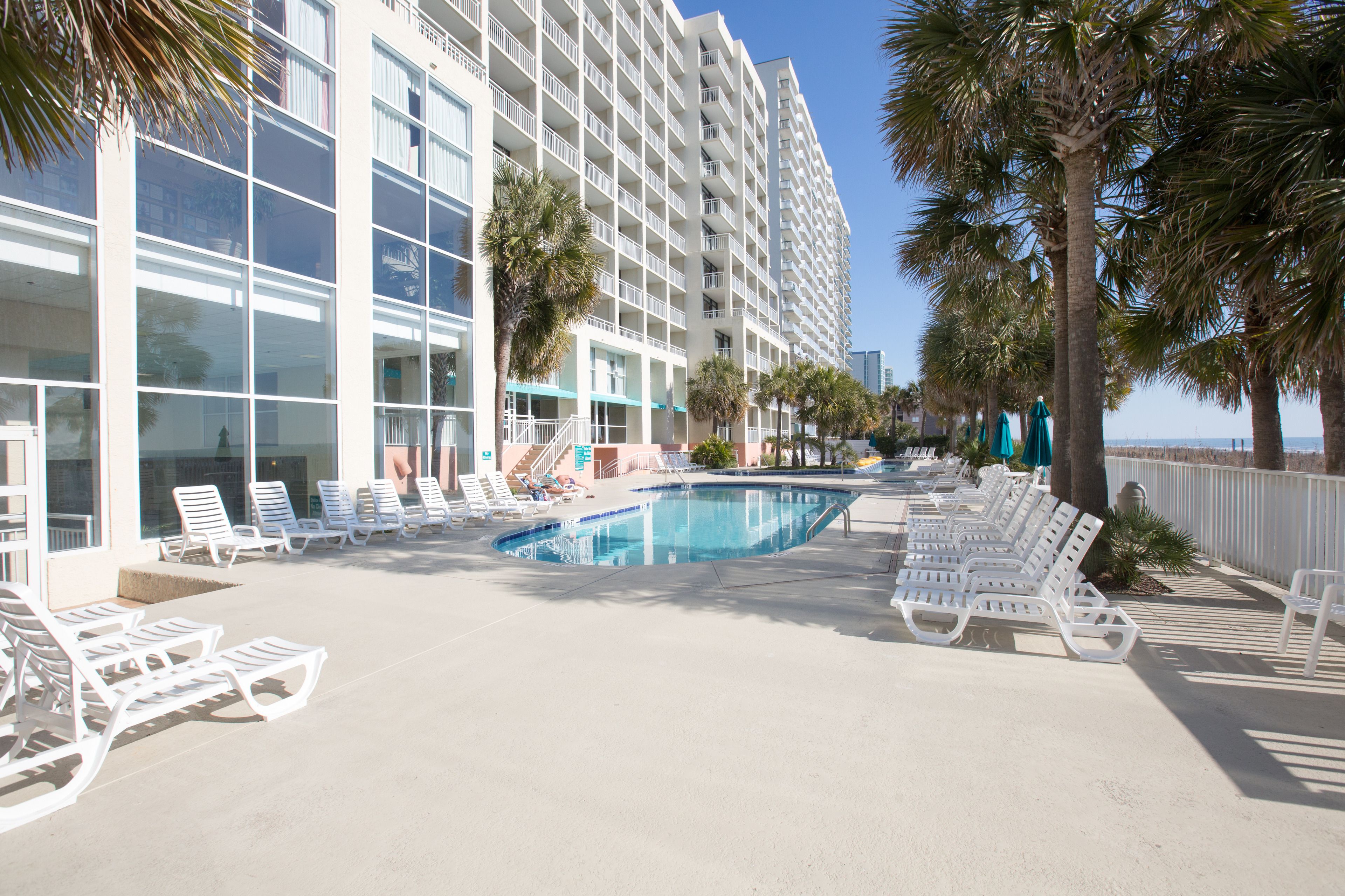 A poolside area with lounge chairs, a swimming pool, and a building with balconies.