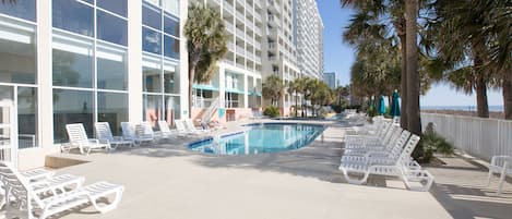 A poolside area with lounge chairs, a swimming pool, and a building with balconies.