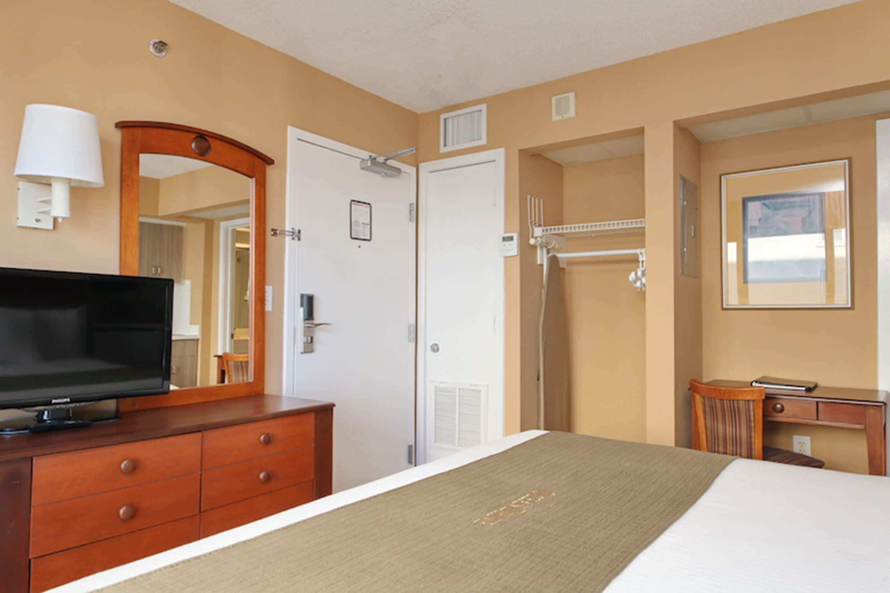 A hotel room with a bed, a television, a dresser, a mirror, a shower, and a desk with a chair.