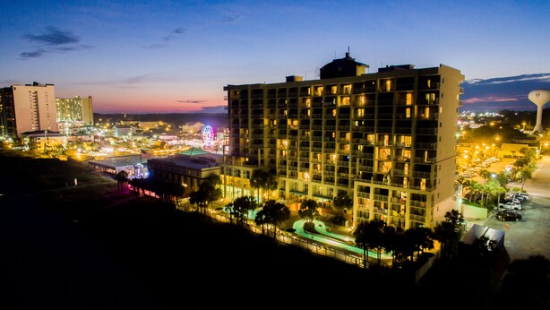 A high-rise hotel with multiple floors, a parking lot, and a large illuminated building in the background. - Ocean Drive Beach & Golf Resort (North Myrtle Beach)