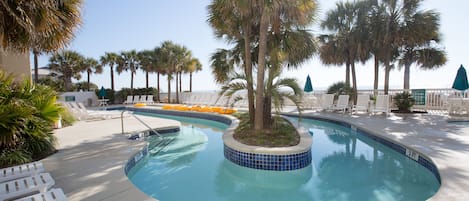 A pool area with a tiled edge, lounge chairs, and palm trees.