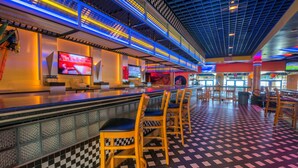 A bar area with checkered floor tiles, bar stools, and a television screen. - Ocean Drive Beach & Golf Resort (North Myrtle Beach)