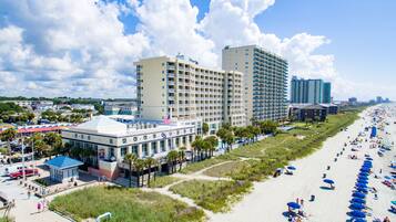 A beachfront hotel with multiple floors, a pool area, and a beach with umbrellas.