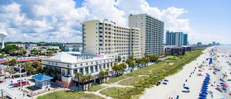 A beachfront hotel with multiple floors, a pool area, and a beach with umbrellas.