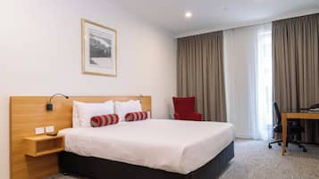 A hotel room with a large bed, a desk, a chair, and a picture on the wall.