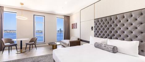 A modern hotel room with a large bed, a view of the city, and a seating area with a table and chairs.