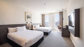 Habitación de hotel con dos camas, un escritorio, televisión y vista a la ciudad.