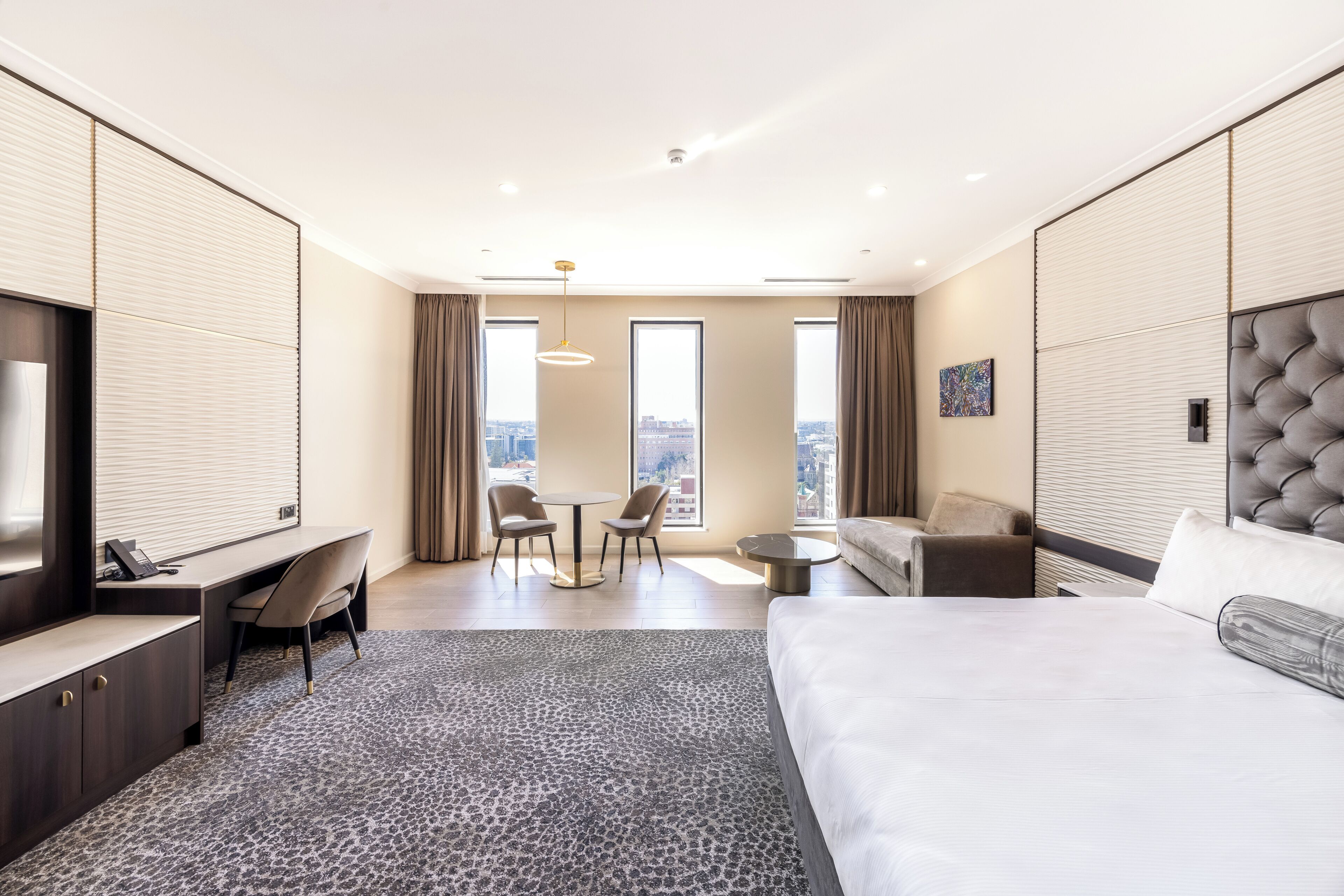 Habitación de hotel con cama, escritorio, sillas, una mesita y ventanas amplias.
