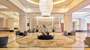 A spacious lobby with a central art installation, seating areas, and a large chandelier.