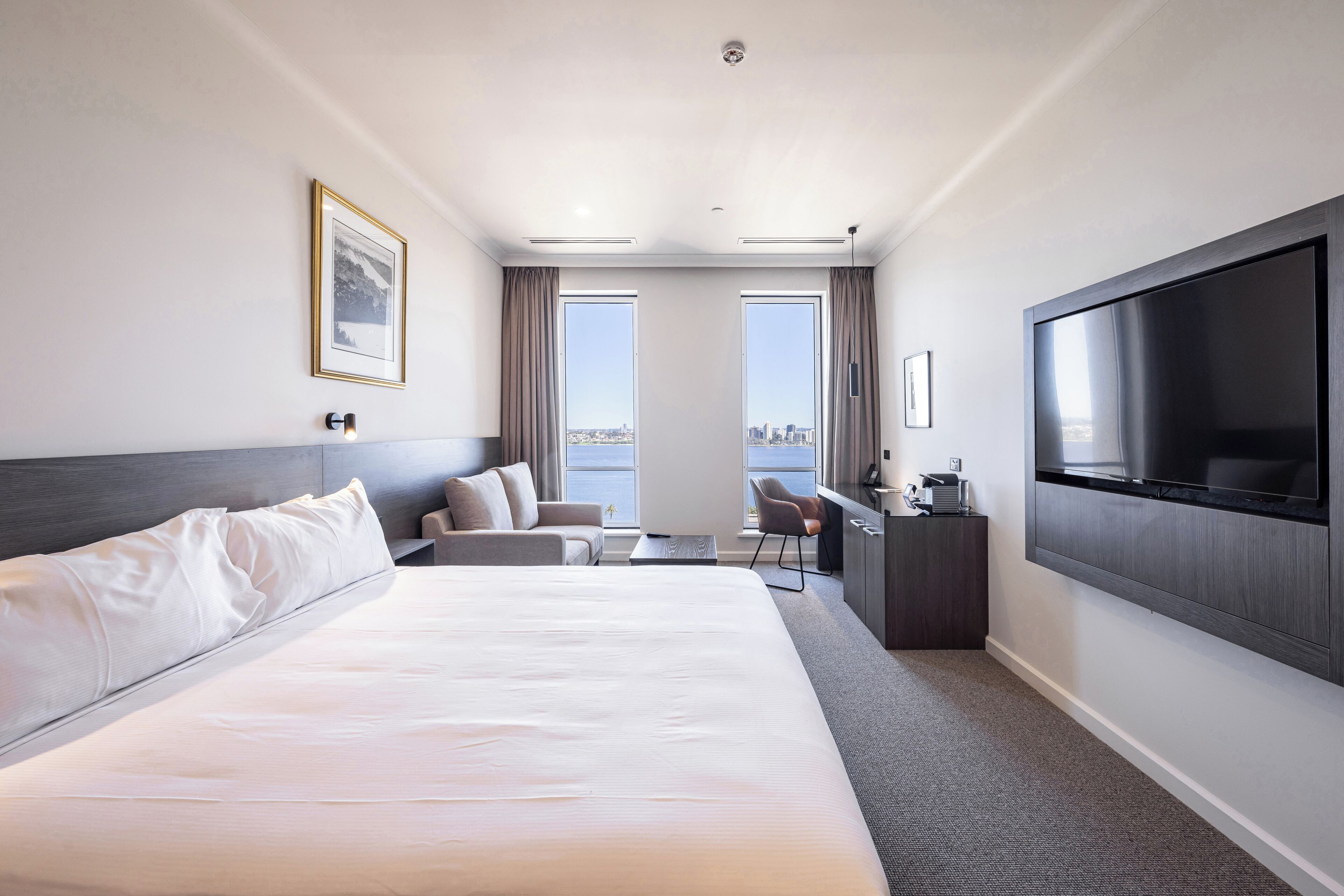 A hotel room with a large bed, a desk, a chair, a TV, and a city view.
