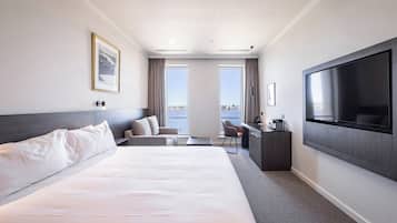 A hotel room with a large bed, a desk, a chair, a TV, and a city view.