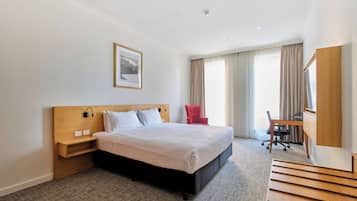 Una habitación de hotel con cama, escritorio, silla y un cuadro en la pared.