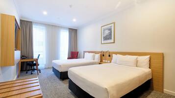 A hotel room with two beds, a desk, a chair, and a large window with curtains.
