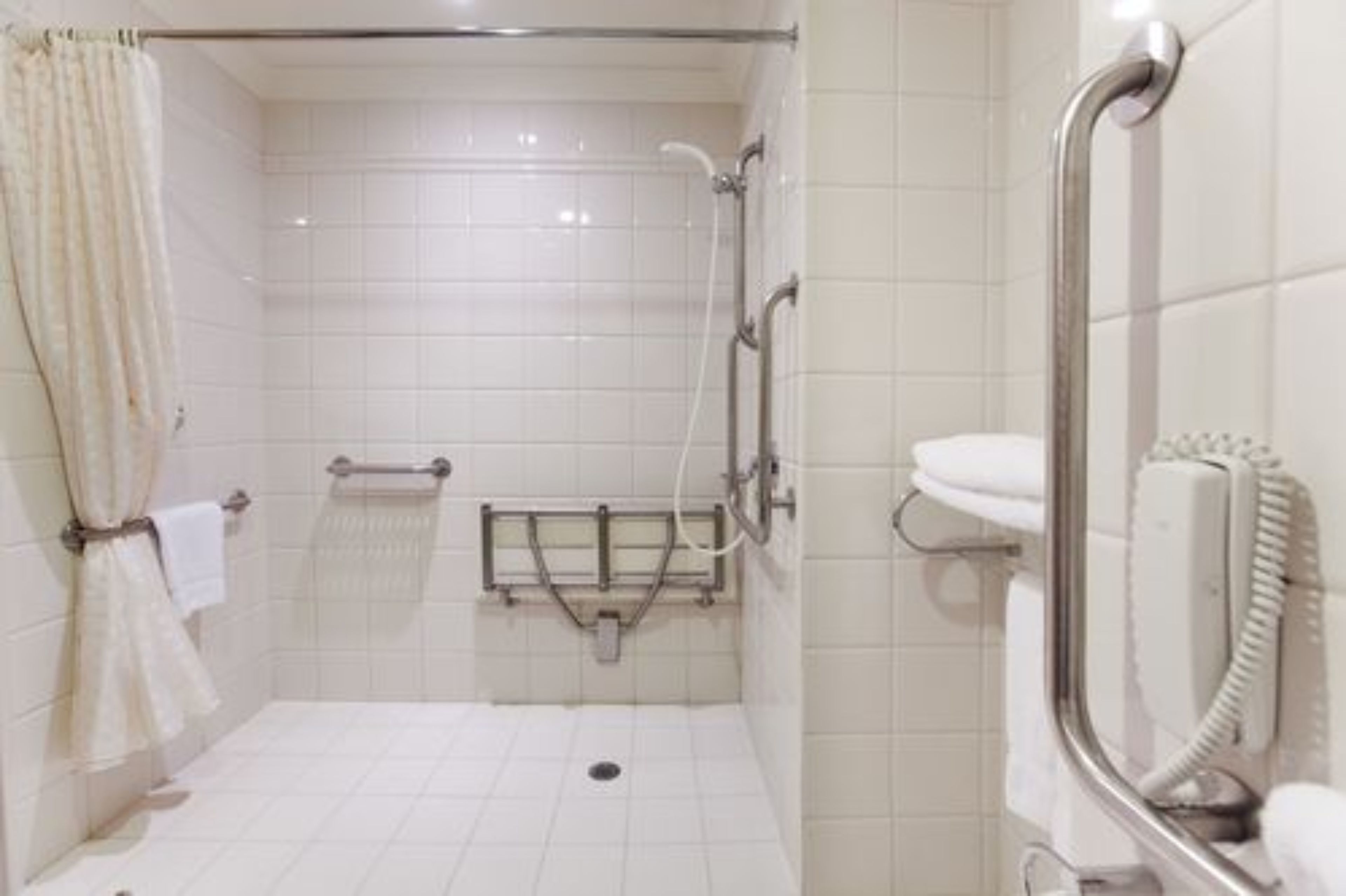 A bathroom with white tiles, a shower with a grab bar, a toilet with a hand dryer, and a towel rack.