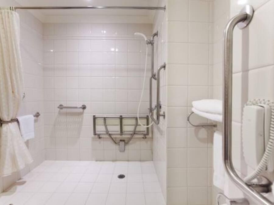 A bathroom with white tiles, a shower with a grab bar, a toilet with a hand dryer, and a towel rack.